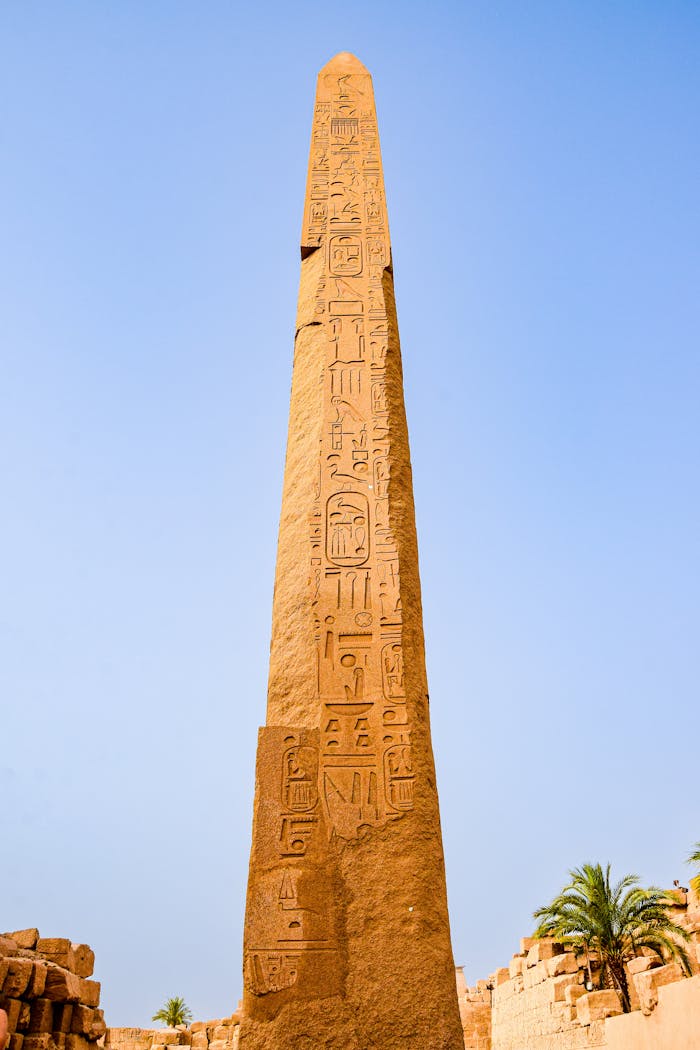 Tall Egyptian obelisk with hieroglyphs under clear blue sky, historical monument.